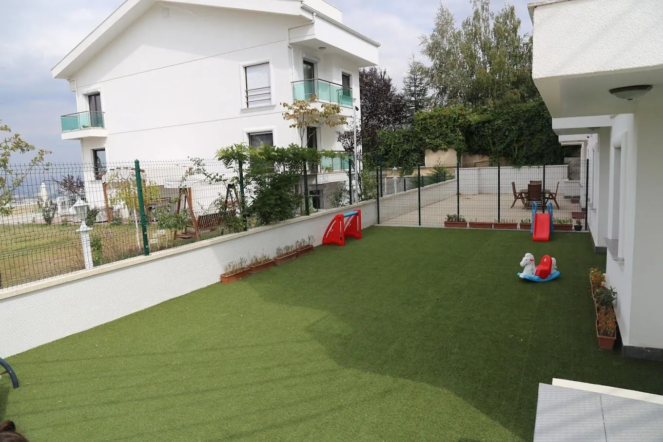 Okulun bahçesi: suni çim alan, salıncak ve oyuncaklar
